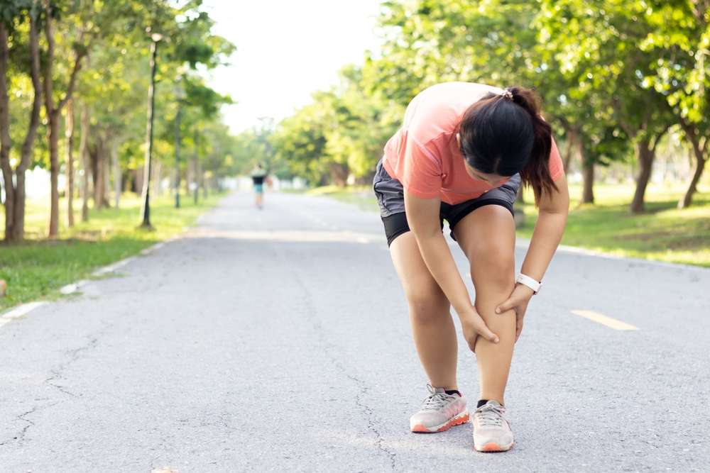 Runner gripping the back of their calf after a sudden tear on a suburban street